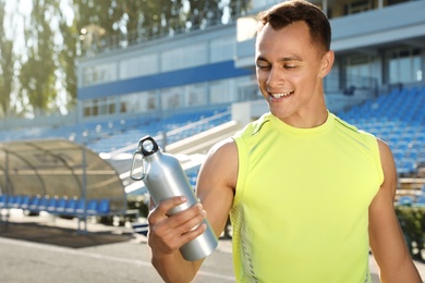 Sporty man with bottle of water at stadium on sunny day. Space for text