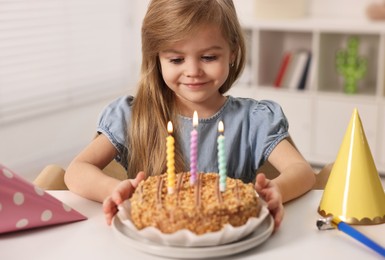 Photo of Cute girl with birthday cake at table indoors