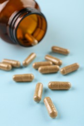 Photo of Bottle and vitamin capsules on light blue background, closeup