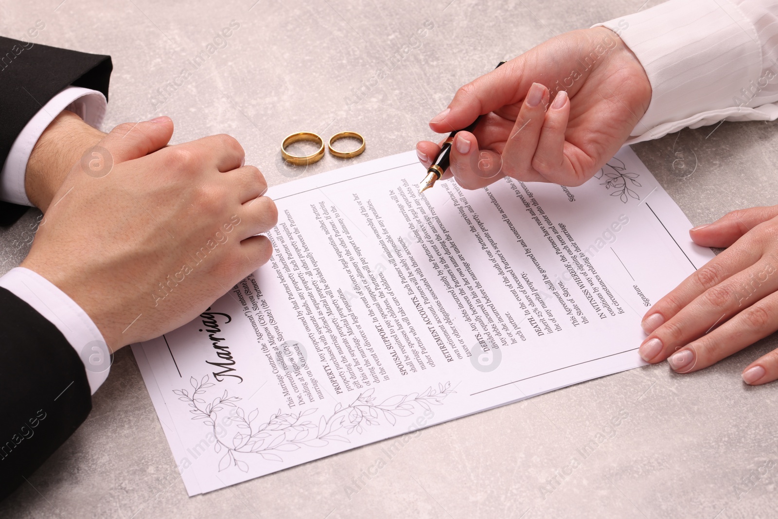 Photo of Man and woman signing marriage contract at light grey table, closeup