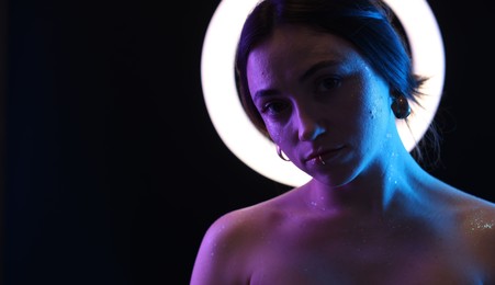 Beautiful woman and ring lamp on dark background in neon lights, space for text