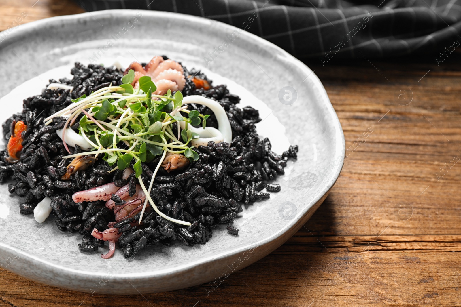 Photo of Delicious black risotto with seafood on wooden table, closeup