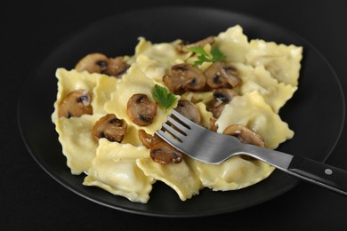 Delicious ravioli with mushrooms and fork on black table, closeup