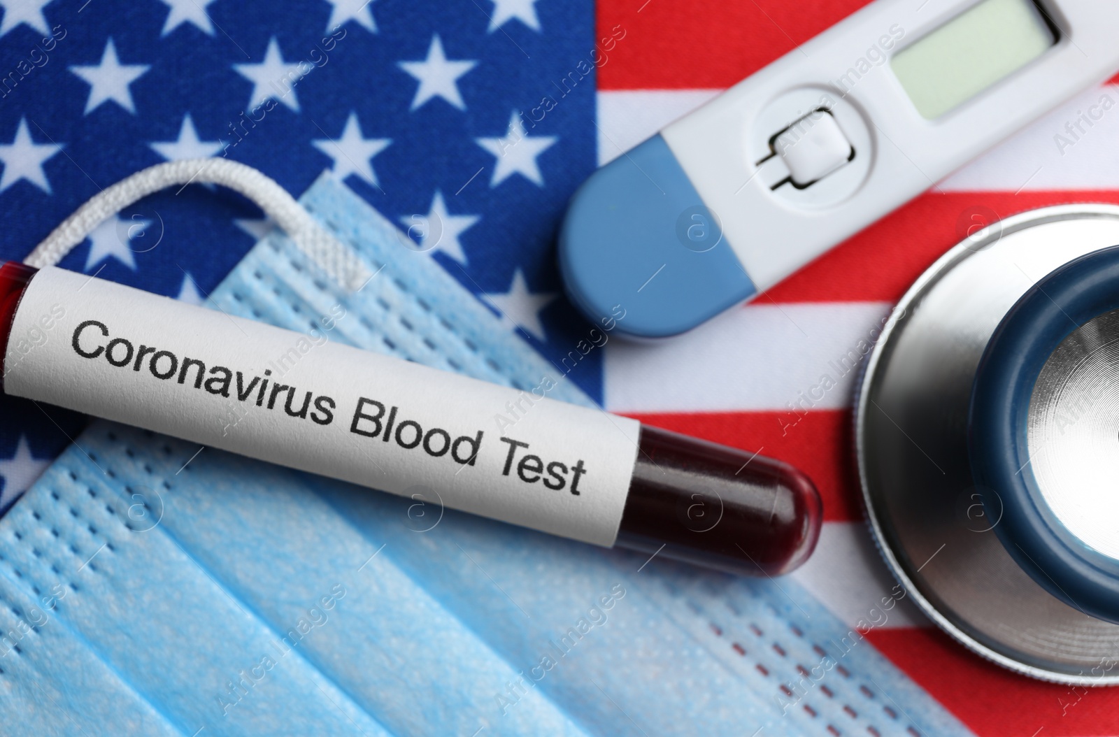 Photo of Test tube with blood sample, medical mask and thermometer on American flag. Coronavirus pandemic in USA