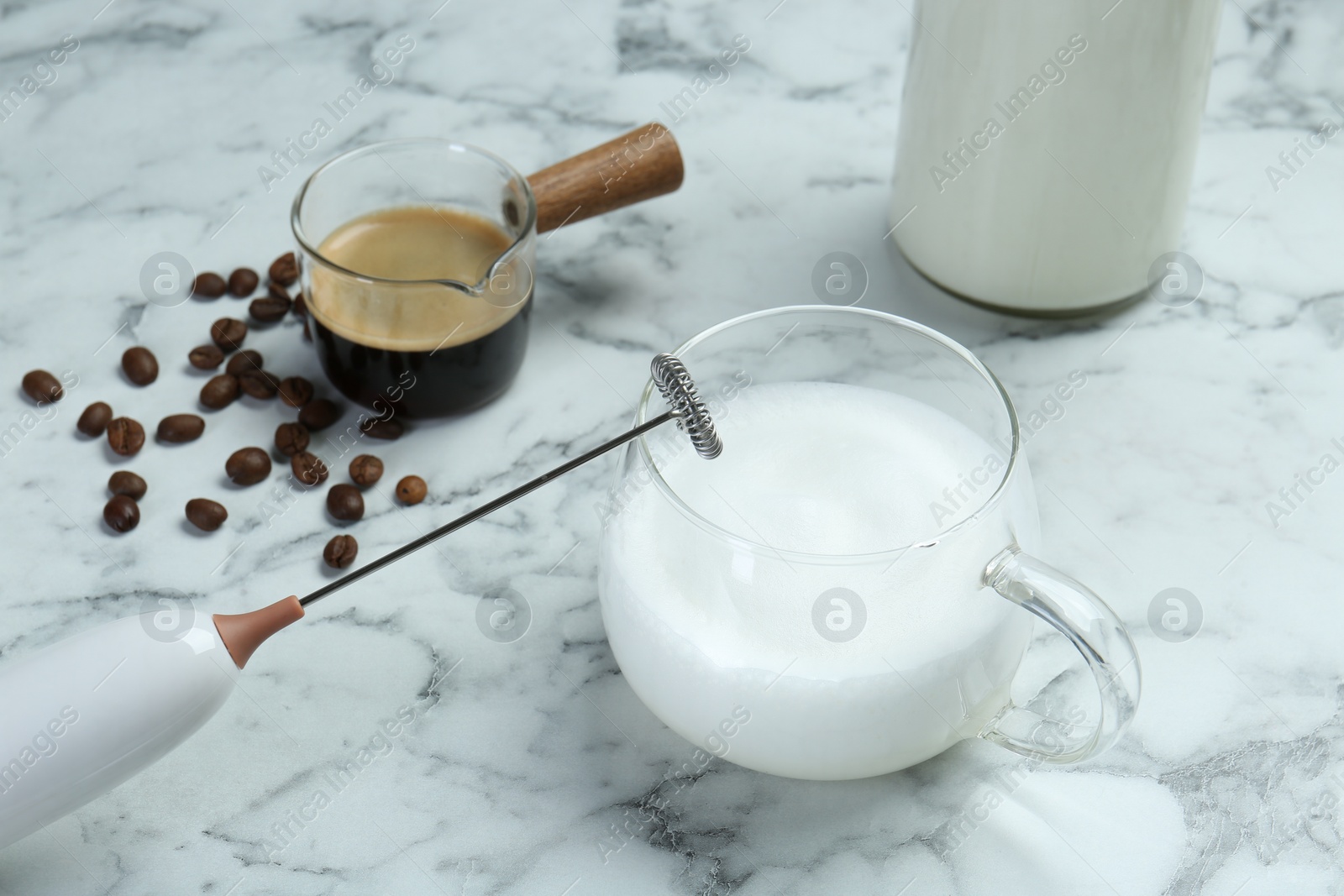 Photo of Mini mixer (milk frother), milk and coffee beans on white marble table, closeup