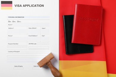 Immigration to Germany. Visa application form, passports and stamp on flag, flat lay