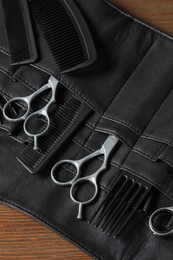 Photo of Hairdresser tools. Professional scissors and combs in leather organizer on wooden table, closeup