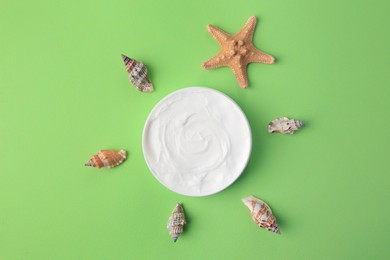 Jar of cream and seashells on light green background, flat lay