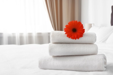 Photo of Stack of fresh towels with flower on bed indoors. Space for text