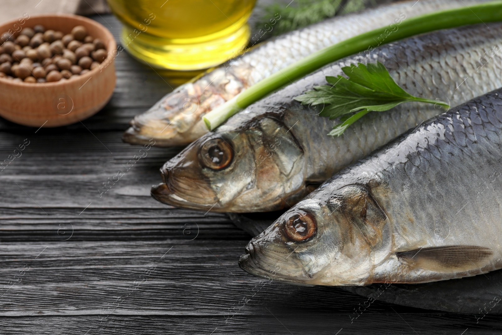 Photo of Delicious salted herrings and ingredients on black wooden table, closeup