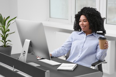 Young woman with cup of drink working on computer at table in office