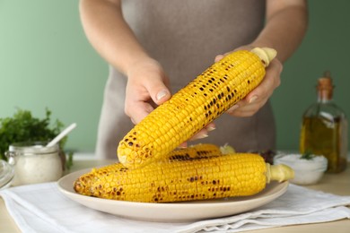 Woman holding tasty grilled corn in kitchen, closeup