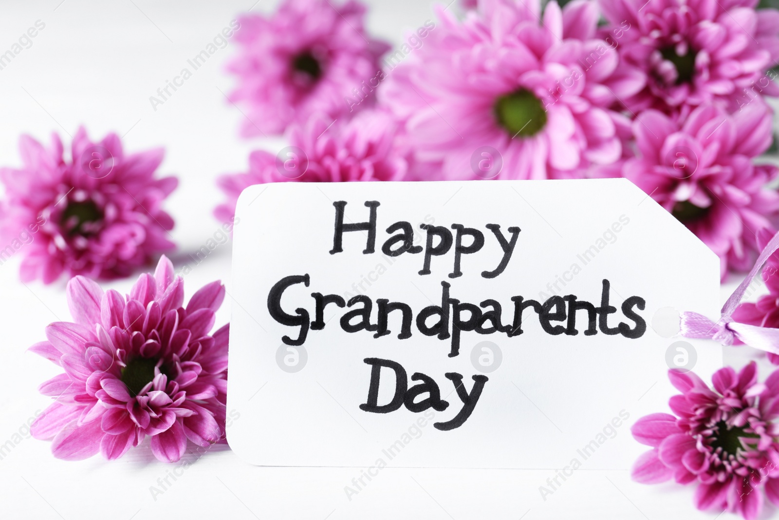 Photo of Beautiful flowers and card with phrase Happy Grandparents Day on white table, closeup