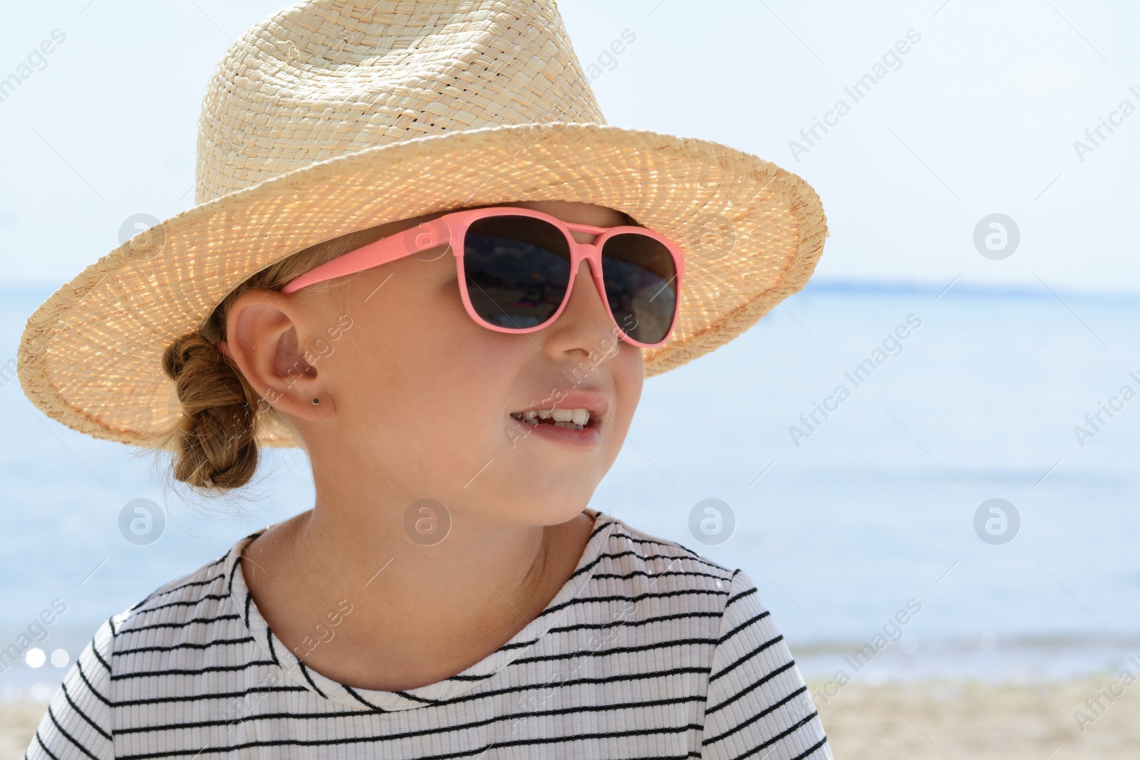 Photo of Little girl wearing sunglasses and hat at beach on sunny day