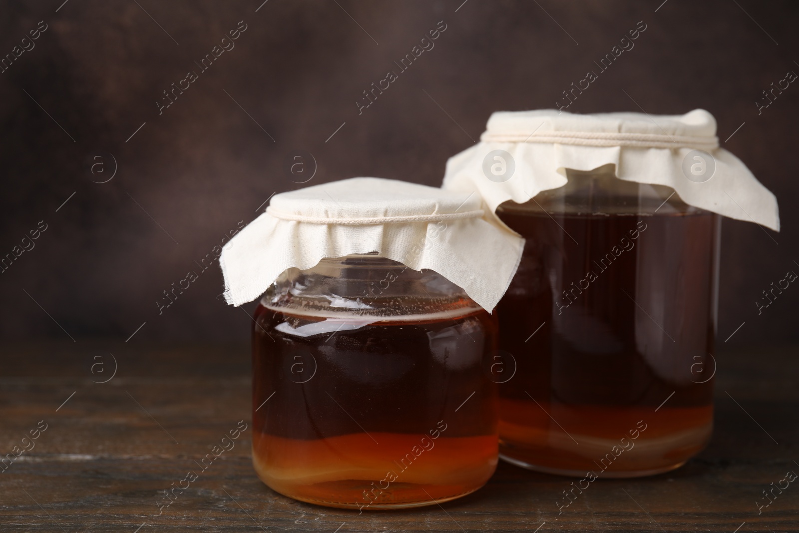 Photo of Tasty kombucha in glass jars on wooden table, space for text