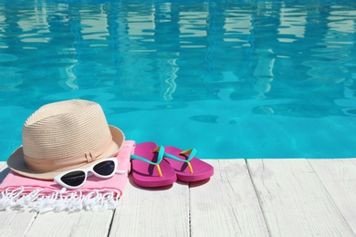 Photo of Beach accessories on wooden deck near swimming pool. Space for text