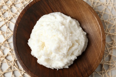 Photo of Shea butter in wooden bowl on wicker mat, top view