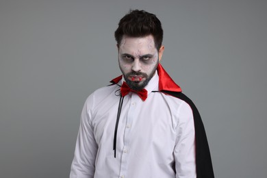 Photo of Man in scary vampire costume with fangs on light grey background. Halloween celebration