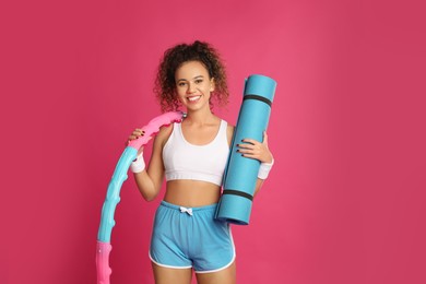 Photo of Beautiful African American woman with yoga mat and hula hoop on pink background