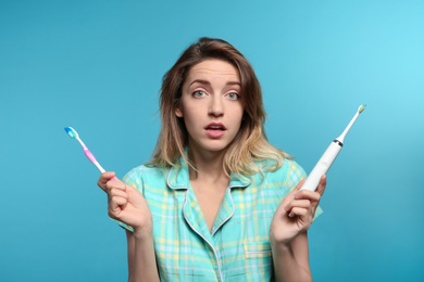 Young woman choosing between manual and electric toothbrushes on color background