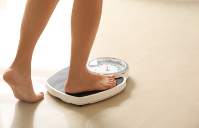 Photo of Woman stepping on floor scales indoors, space for text. Overweight problem
