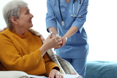 Photo of Care worker giving water to elderly woman in geriatric hospice