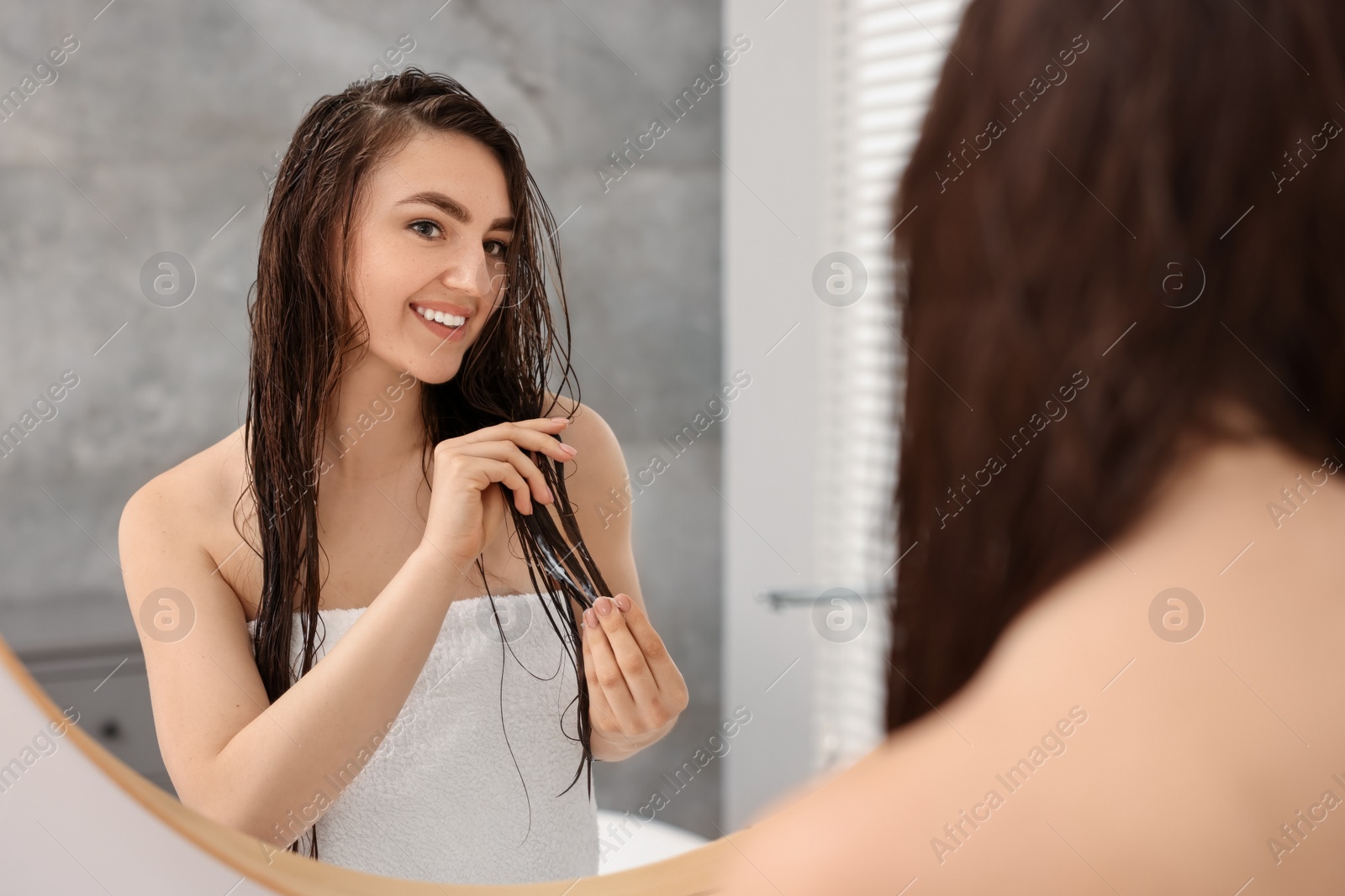 Photo of Young woman applying hair mask near mirror in bathroom