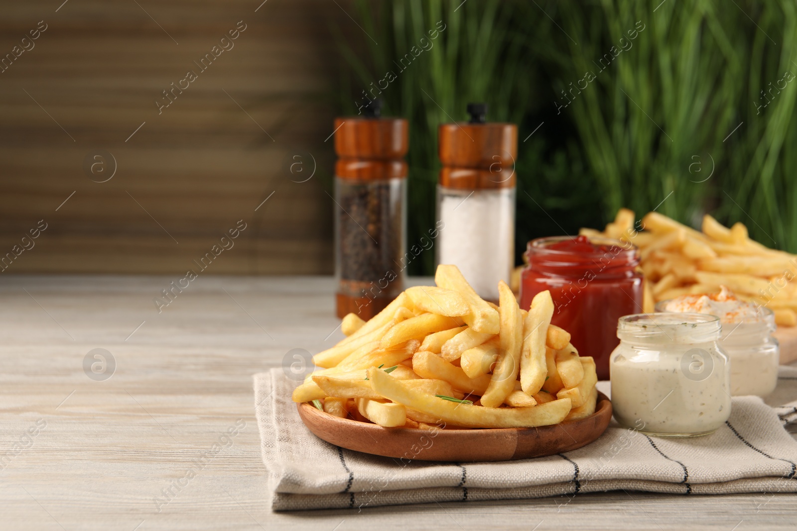 Photo of Delicious french fries served with sauces on light wooden table. Space for text