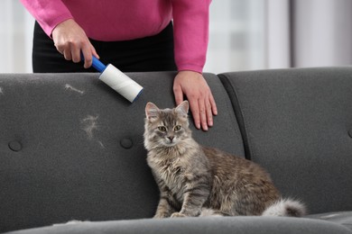 Pet shedding. Woman with lint roller removing cat`s hair from sofa at home, closeup