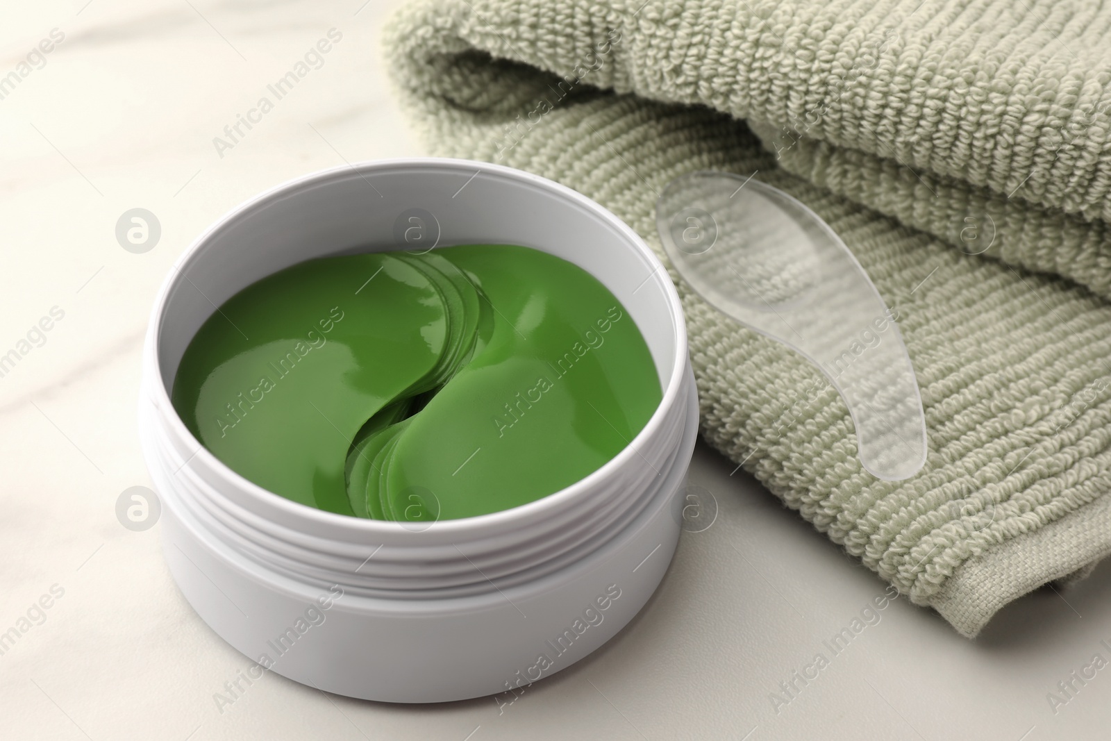 Photo of Jar of under eye patches with spoon and towel on white background, closeup. Care products