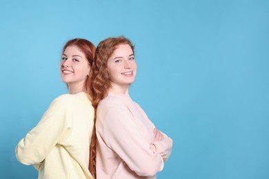 Portrait of beautiful young redhead sisters on light blue background. Space for text