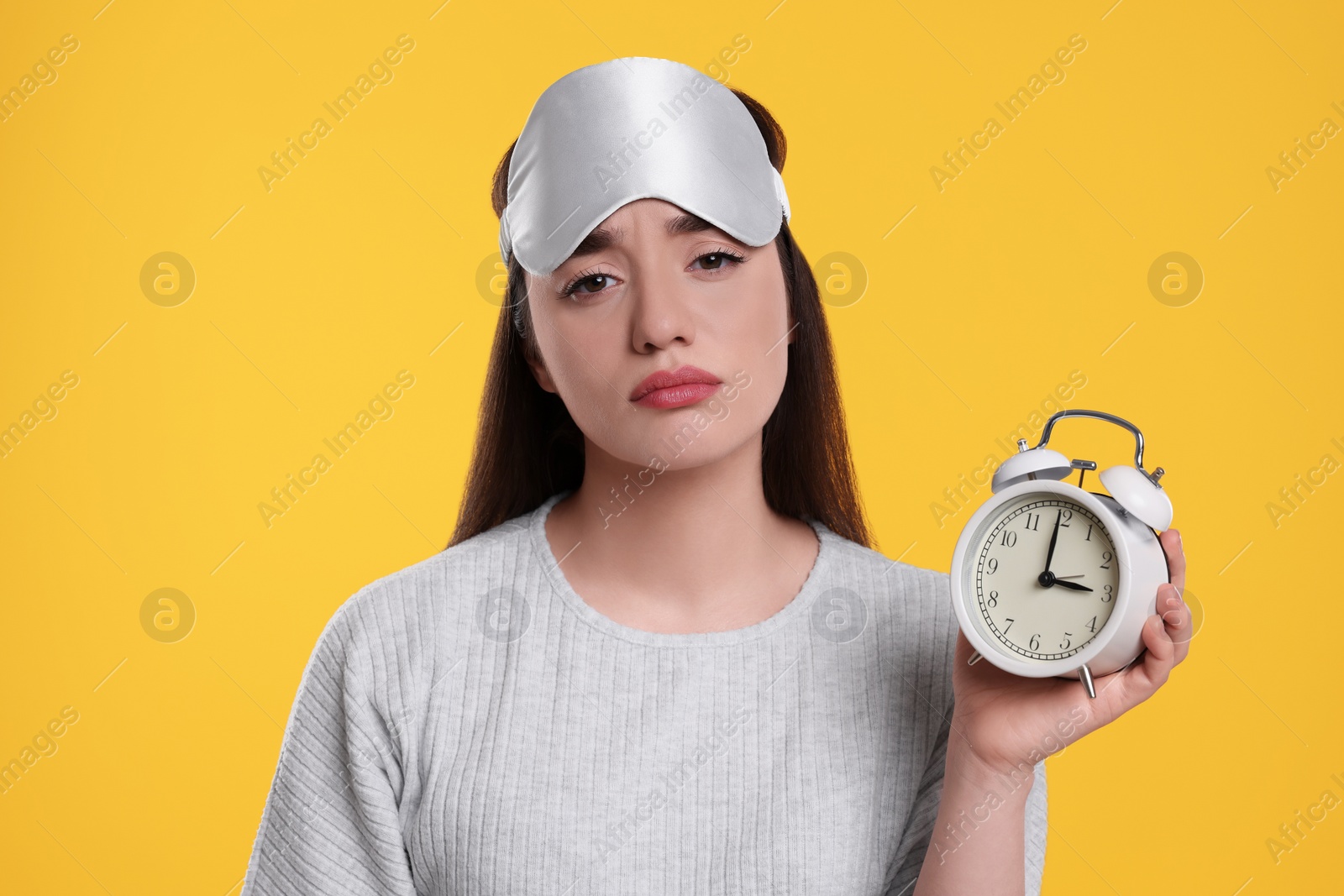 Photo of Tired young woman with sleep mask and alarm clock on yellow background. Insomnia problem