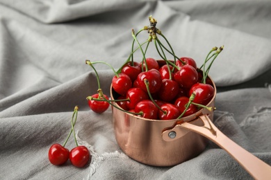 Photo of Saucepan with sweet red cherries on fabric