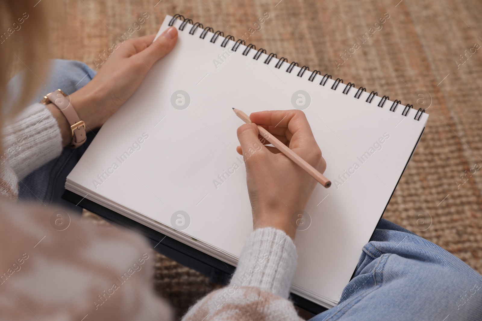 Photo of Woman drawing in sketchbook with pencil on floor at home, above view