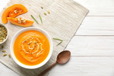 Flat lay composition with bowl of pumpkin soup and space for text on wooden table