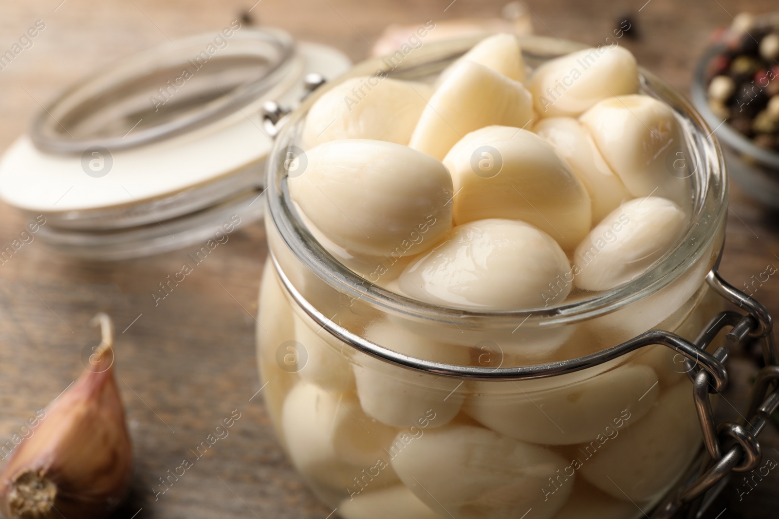 Photo of Preserved garlic in glass jar on wooden table, closeup