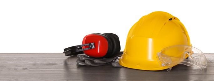 Photo of Hard hat, earmuffs, gloves and goggles on wooden table against white background. Safety equipment