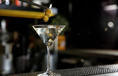 Photo of Adding olives to glass of martini cocktail on bar counter. Space for text
