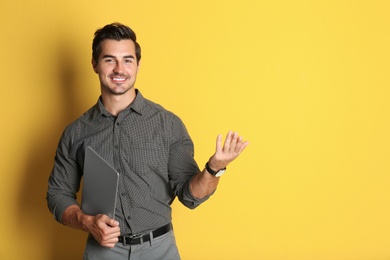 Young male teacher with laptop on yellow background. Space for text