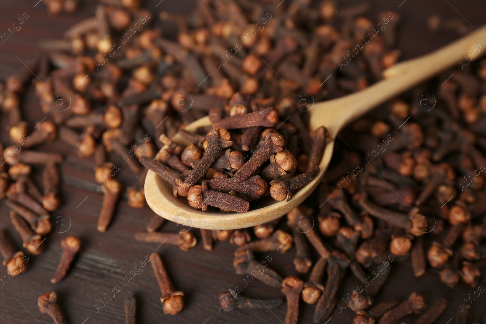 Photo of Spoon and aromatic dry cloves on wooden table, closeup