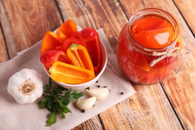 Photo of Jar of pickled bell peppers, parsley, peppercorns and garlic on wooden table