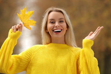Portrait of happy woman with autumn leaf outdoors