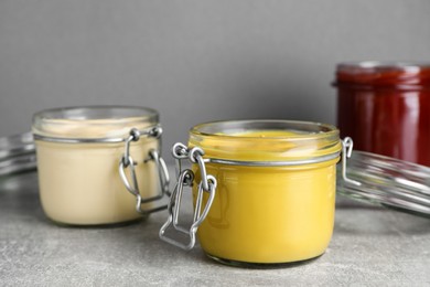 Photo of Jars with mustard, mayonnaise and ketchup on light grey table, closeup