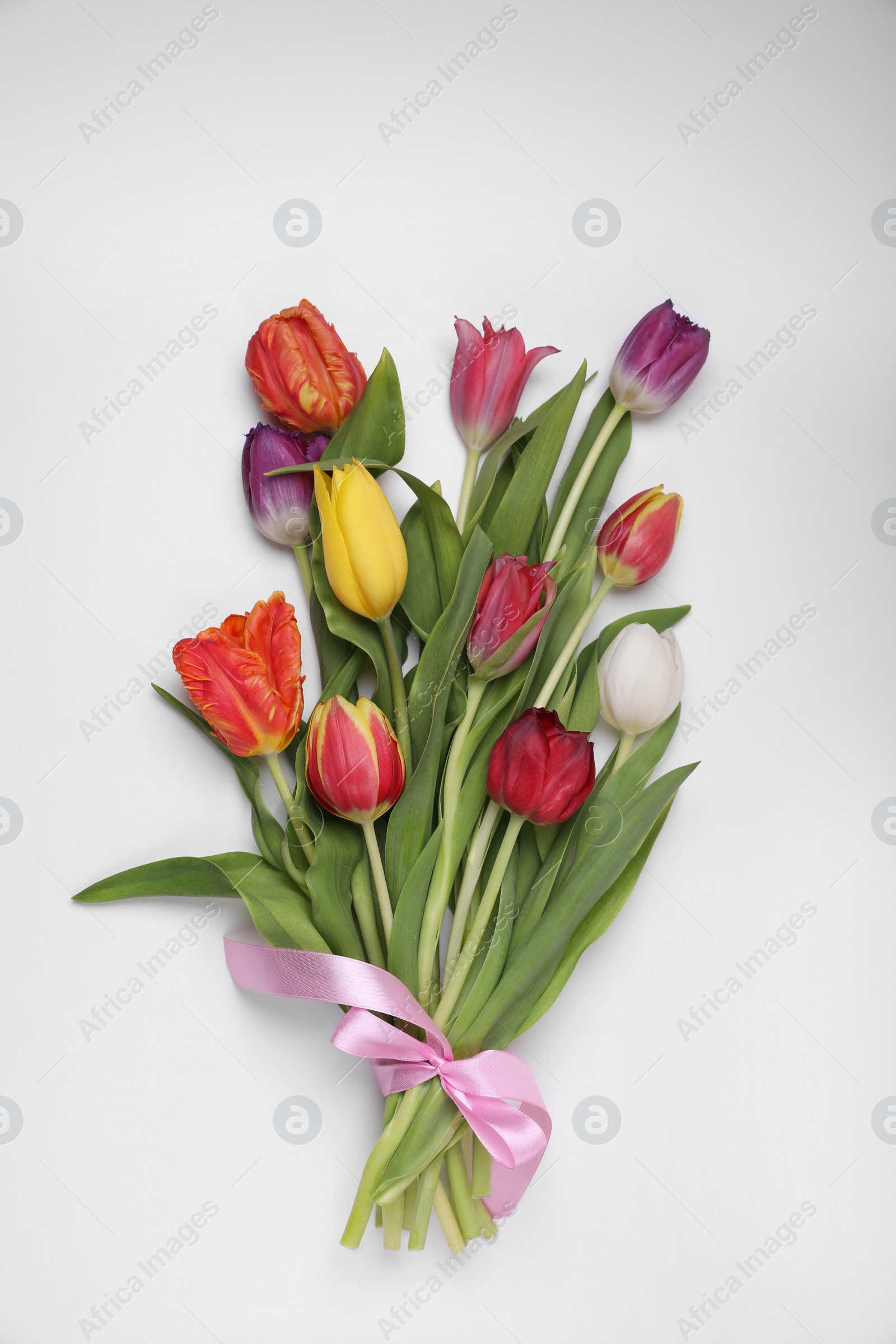 Photo of Bouquet of beautiful colorful tulips tied with pink ribbon on white background, top view