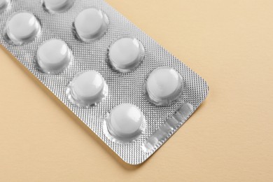 Photo of White pills in blister on beige background, closeup