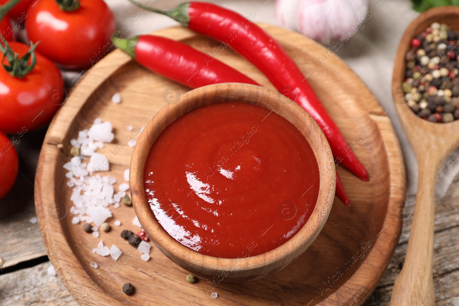 Photo of Delicious ketchup in bowl, chili pepper and spices on wooden table, closeup. Tomato sauce