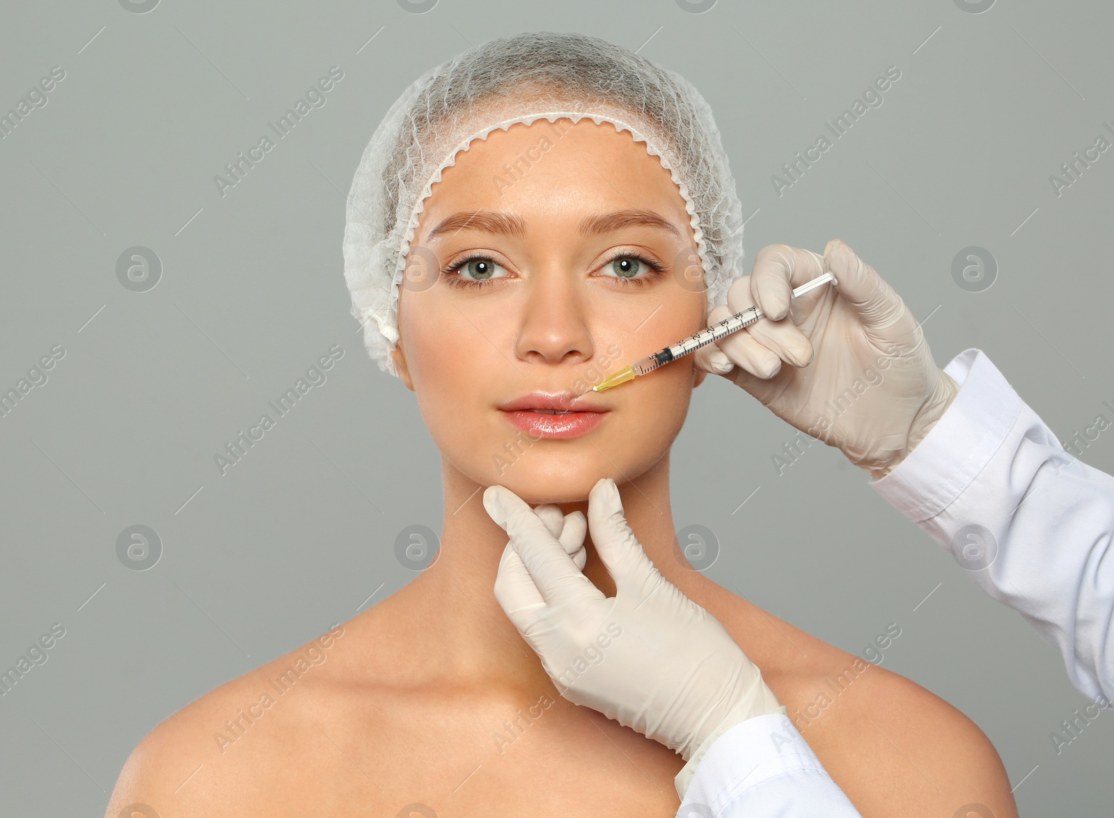 Photo of Young woman getting lips injection on grey background. Cosmetic surgery