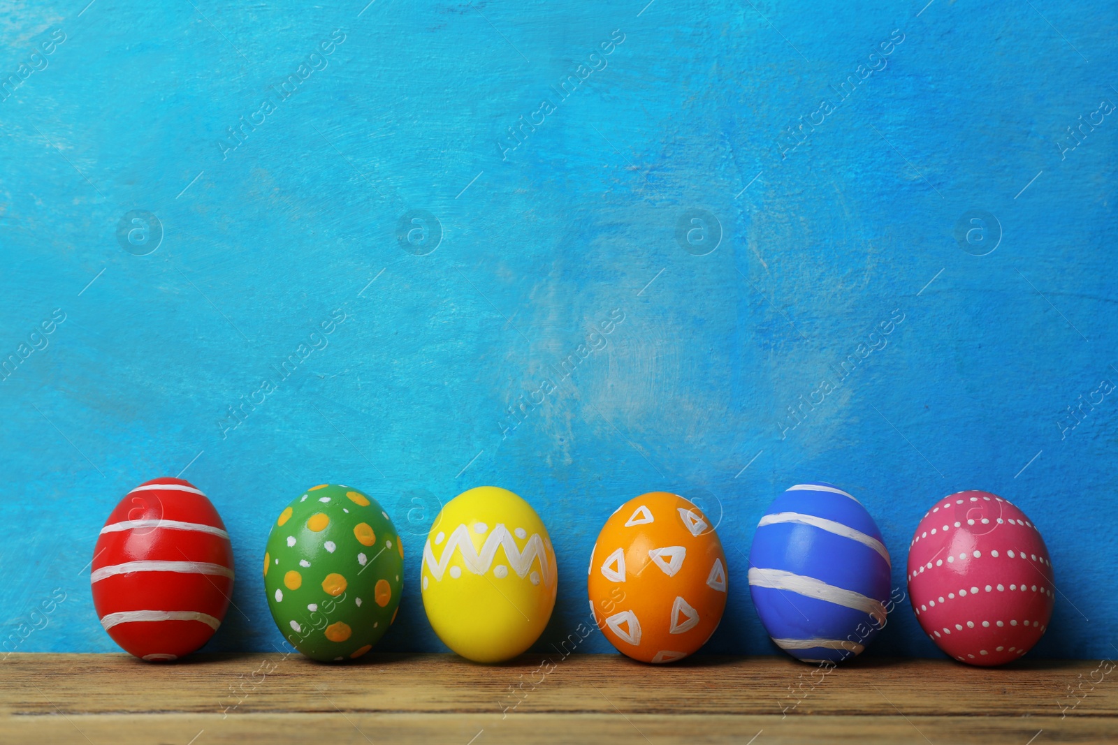 Photo of Decorated Easter eggs on table near color wall. Space for text