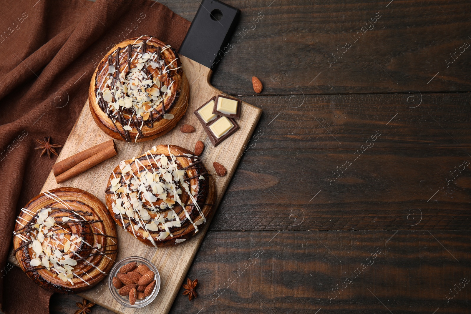 Photo of Sweet buns. Delicious rolls with toppings, almond and spices on wooden table, top view. Space for text