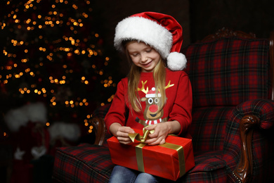 Photo of Cute little child with Christmas gift sitting in armchair at home